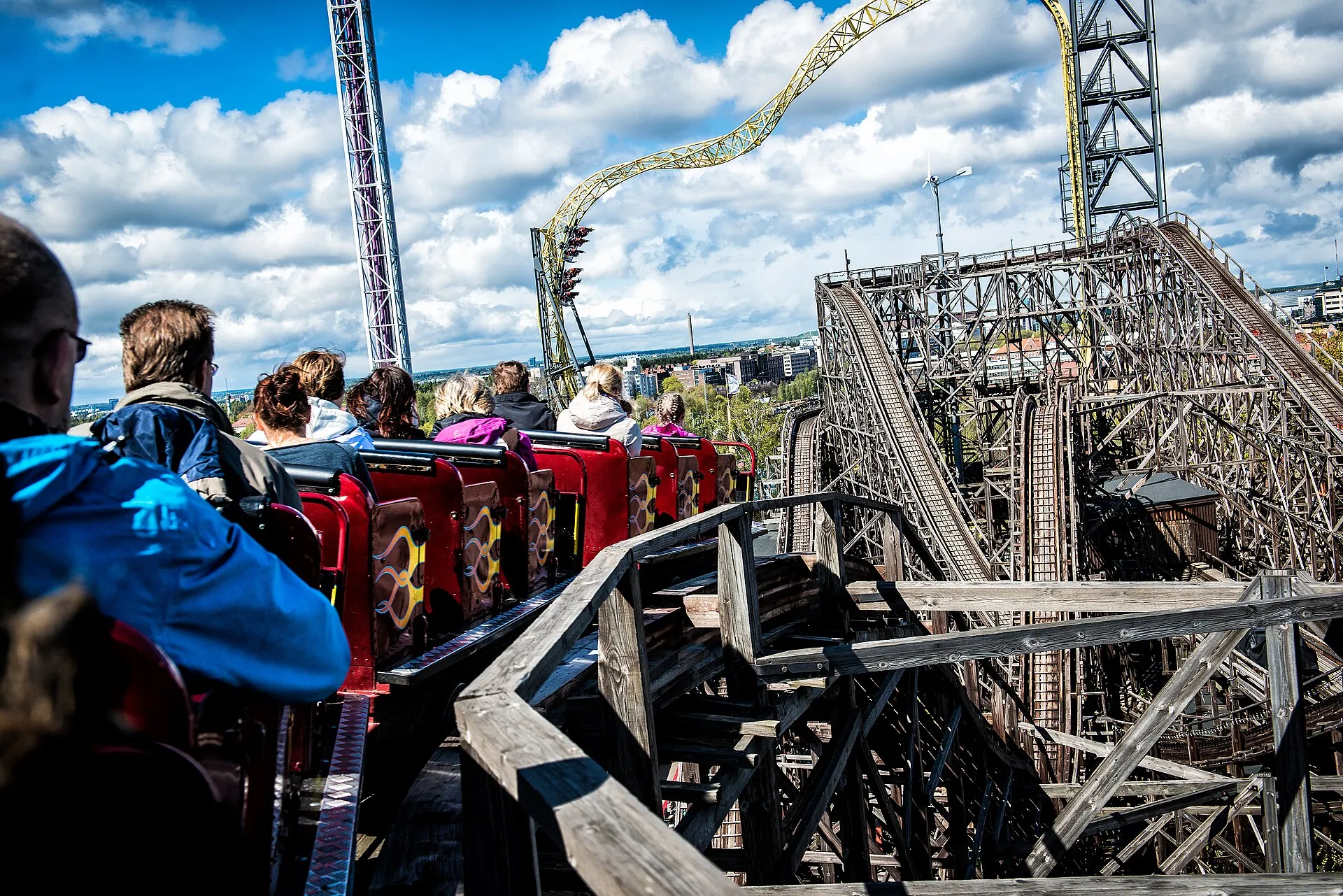 Riders on the wooden Vuoristorata roller coaster at Linnanmäki with the Helsinki skyline behind