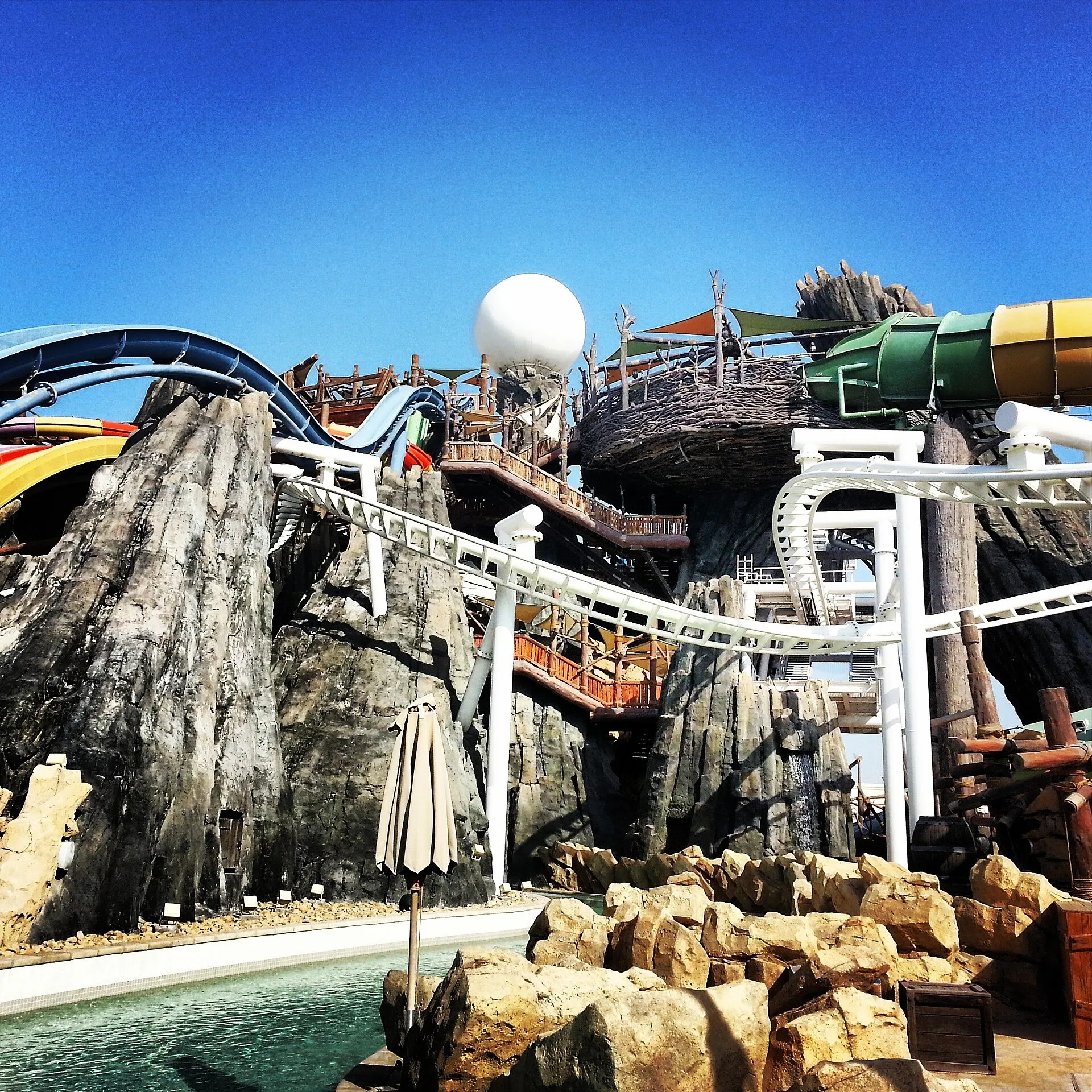 Waterslides and rock work at Yas Waterworld Abu Dhabi, with the Dawwama funnel and Bandit Bomber coaster track