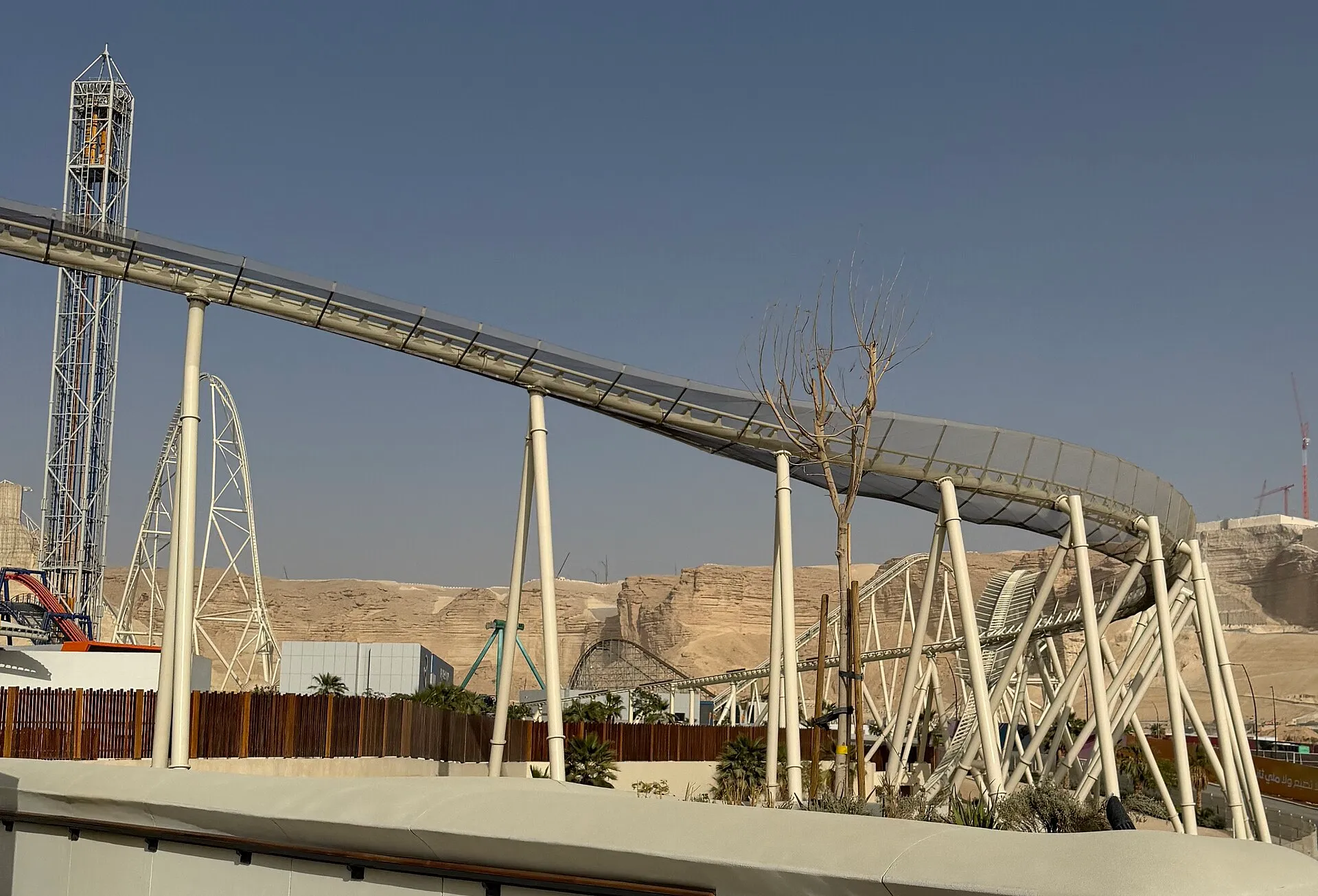 Falcon's Flight roller coaster track curving above Six Flags Qiddiya City with the Tuwaiq cliffs behind