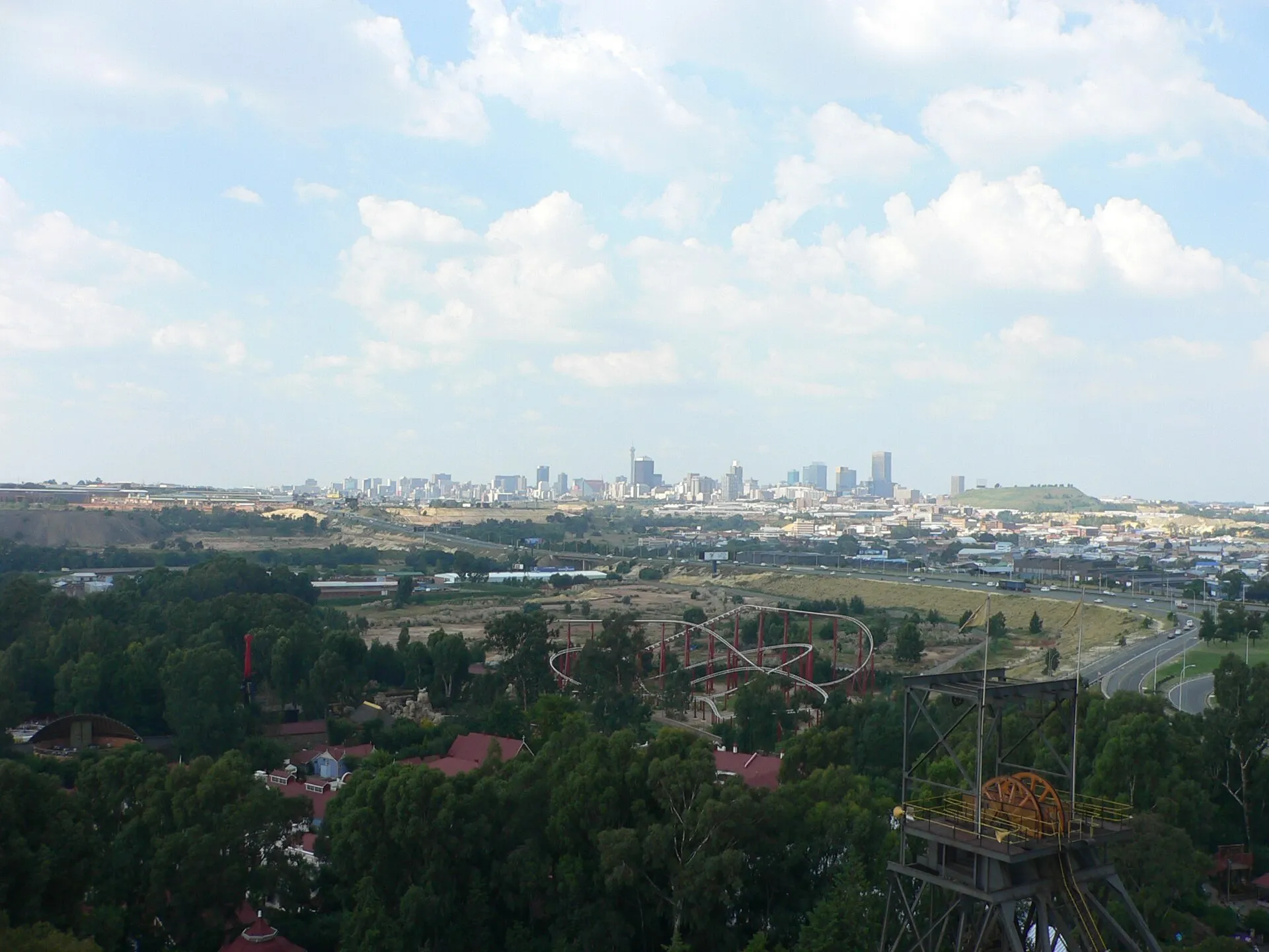 View over Gold Reef City theme park with the Anaconda roller coaster, historic mine headgear and the Johannesburg skyline behind