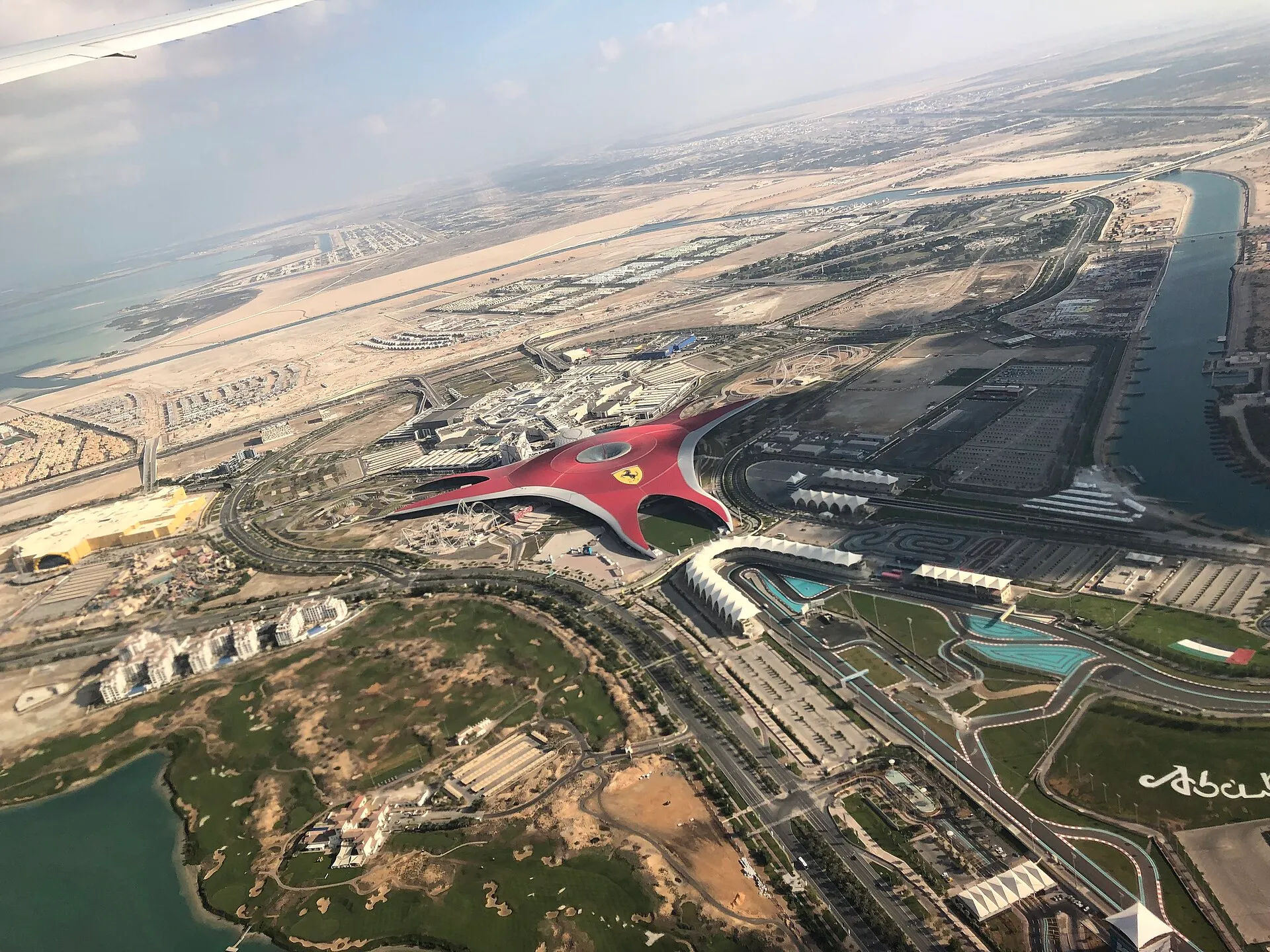 Aerial view of Ferrari World Abu Dhabi's red star-shaped roof on Yas Island, with Yas Marina Circuit alongside